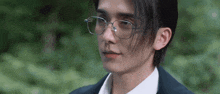 a man wearing glasses and a suit is looking at the camera .