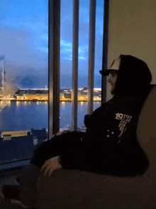 a man wearing a hoodie with the number 19 on it sits in front of a large window