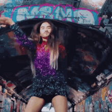 a man in a purple sequined dress is dancing in front of a wall that has graffiti on it