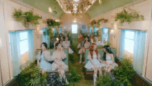 a group of girls are sitting in a train car surrounded by plants and flowers .
