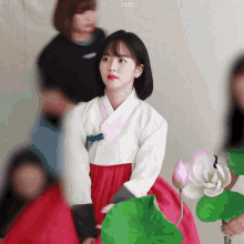 a woman in a traditional korean dress is sitting next to a flower
