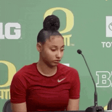 a woman in a red nike shirt is sitting at a table in front of a microphone .