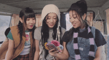 three girls are looking at a cell phone and one has a flower in her hair