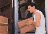a man in a white tank top is carrying a cardboard box