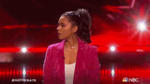 a woman is standing on a stage wearing a pink jacket and a white shirt .