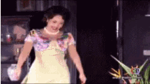 a woman in a yellow dress is standing in front of a tv screen