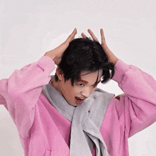 a person wearing a pink sweater and a grey scarf holds their hands to their head