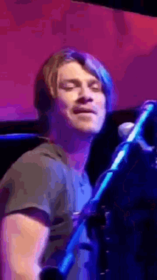 a man singing into a microphone with his eyes closed in front of a purple background