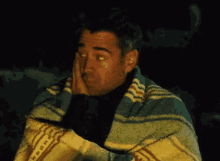 a man wrapped in a blanket with his hand on his face .