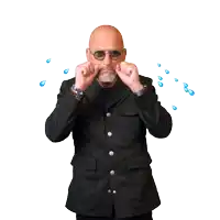 a bald man wearing sunglasses and a black jacket is covering his ears with his hands
