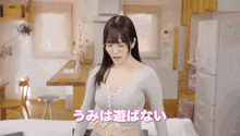 a woman in a grey sweater is sitting on a bed in a room with chinese writing on the bottom