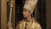 a man in a gold robe and hat is holding a gold pole