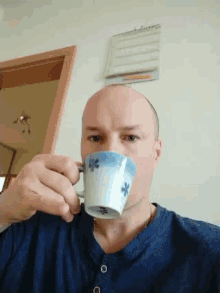 a bald man drinks from a blue and white cup with snowflakes on it