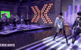 a group of young men are performing on a stage with a large x behind them