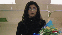 a woman with glasses holds a bouquet of flowers in front of a sign that says full