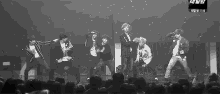 a black and white photo of a group of people dancing on a stage in front of a crowd .