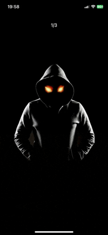 a man in a hoodie with glowing eyes is standing in the dark on a cell phone screen .