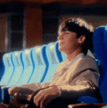 a young man is sitting in a row of blue seats in a theater .