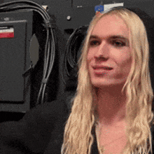 a woman with long blonde hair is standing in front of a wall with wires hanging on it