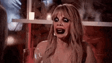 a woman with black lipstick on her face is holding a glass of wine and making a funny face .