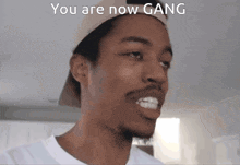 a man wearing a hat with the words you are now gang on the bottom