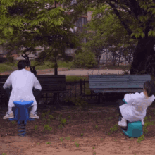 a man sits on a blue seesaw while another sits on a green stool