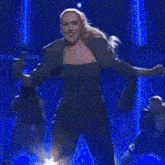 a woman in a suit is dancing on a stage with her arms outstretched in front of a crowd .