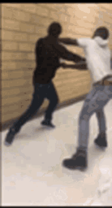 two men are fighting each other in a hallway in front of a brick wall .