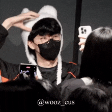 a man wearing a mask and a furry hat is taking a picture of himself with a cell phone .