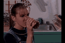 a young girl is drinking from a glass in front of a kitchen sink .
