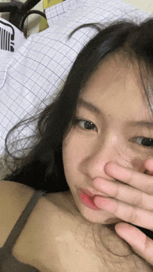 a girl covering her face with her hand with a puma shirt on the bed in the background