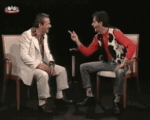 a man in a cow print vest is talking to another man in a chair