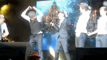 a group of men in suits are dancing on a stage in front of a chandelier