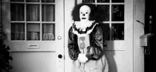 a black and white photo of a clown standing in front of a white door