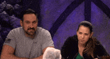 a man and a woman are sitting at a table and the man is wearing an under armour shirt