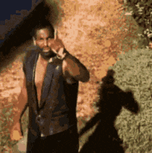 a man without a shirt is talking on a cell phone and his shadow is visible