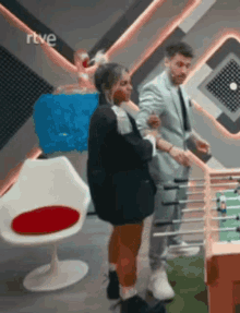 a man and a woman are playing foosball in a room with a rtve logo in the background .
