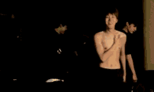 a man without a shirt is standing in a dark room with his hands on his chest .
