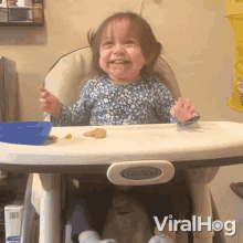 a little girl is sitting in a graco high chair and smiling