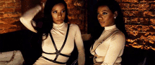 two women are sitting next to each other on a couch . one of the women is wearing a harness .