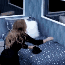 a woman is standing next to a bed with a blue blanket and pillows .
