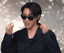 a man wearing sunglasses and a black jacket is smiling