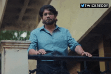 a man in a blue shirt is standing on a balcony with a wickreddy sticker above him