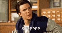 a man in a varsity jacket is sitting in a room and making a face .