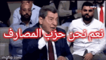 a man in a suit and tie is sitting in front of a group of people with arabic writing on them .