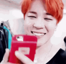 a man with red hair is smiling while holding a red cell phone in his hand .