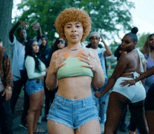 a woman in a green crop top and shorts is surrounded by people
