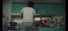 a man in a white shirt is standing in a kitchen talking on a cell phone