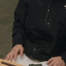 a man is sitting at a table with chopsticks and a cell phone in his hand .