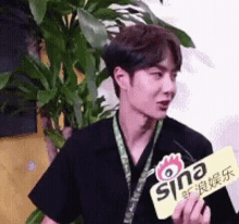 a man in a black shirt is holding a yellow sign that says sina on it .